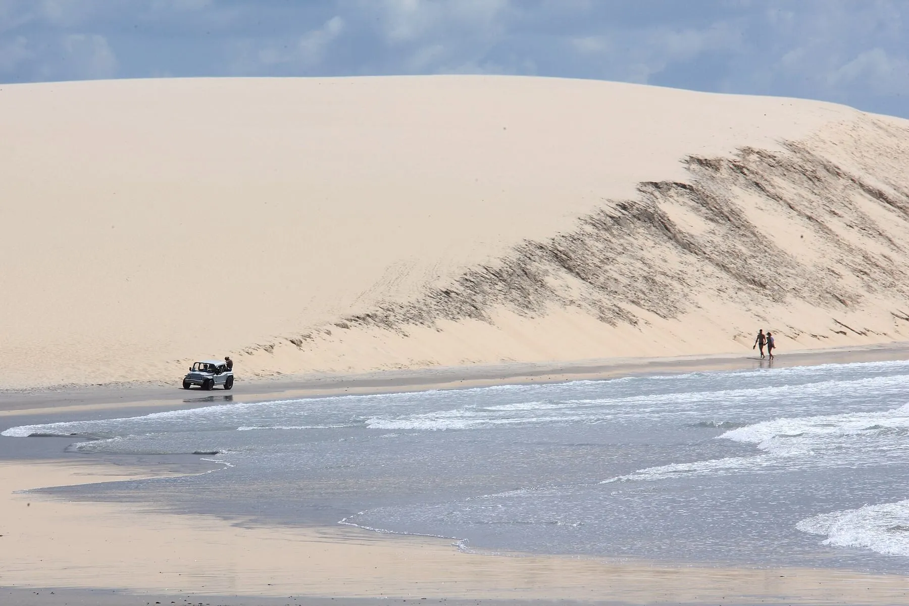 4x4 vehicle crossing sand at the foot of a large dune by the seaside