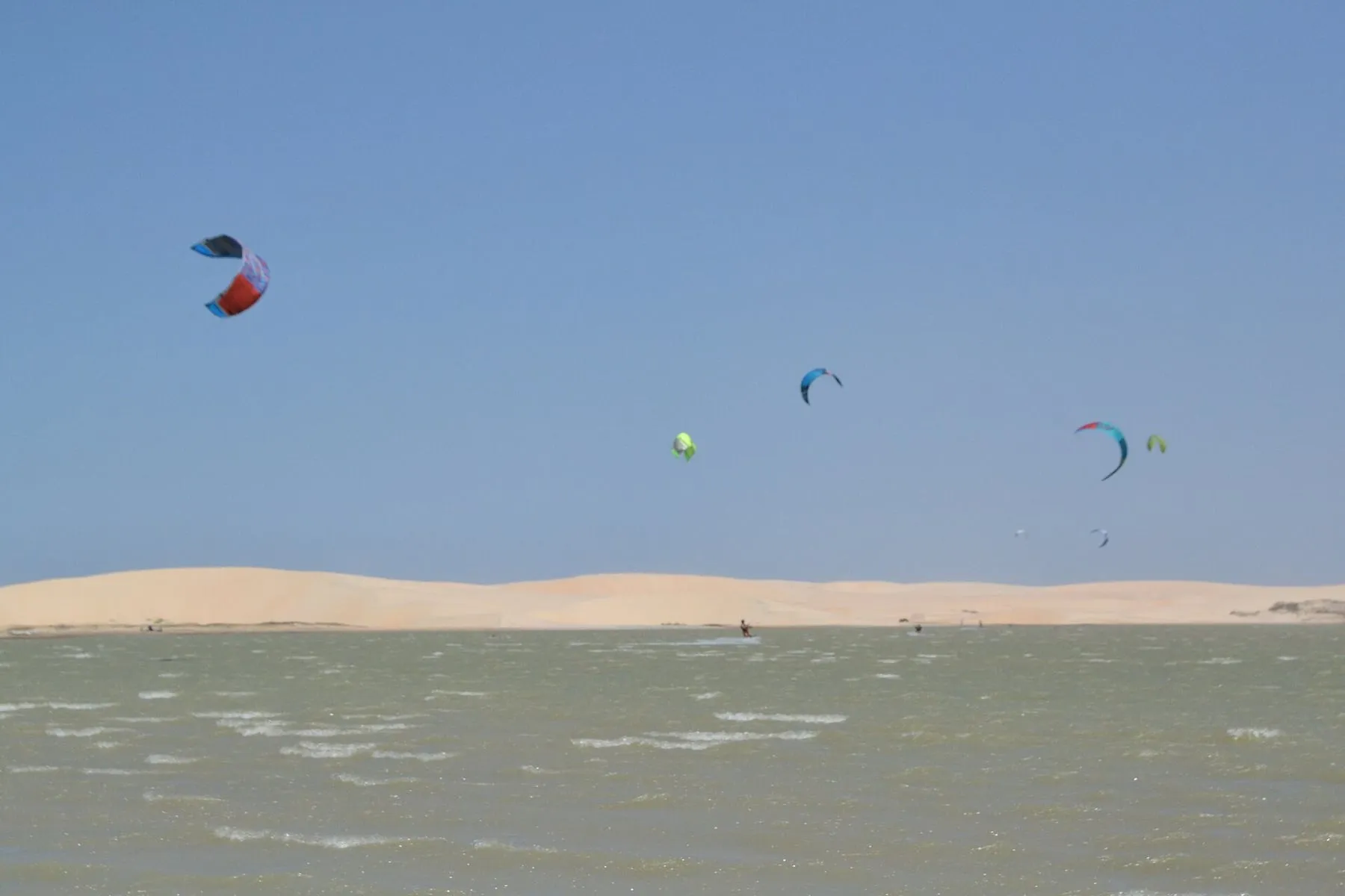 Mehrere Kitesegel über einer flachen Lagune, umgeben von Dünen