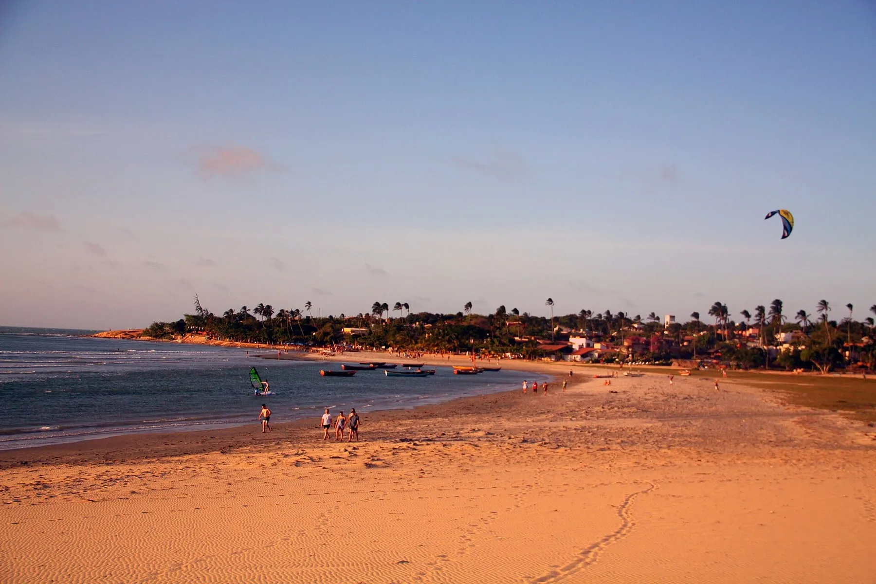 Jericoacoara village viewed from the beach at sunset, with coconut trees and a kite in the sky